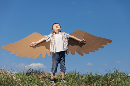 Little boy playing with cardboard toy wings in the park at the day time. Concept of happy game. Child having fun outdoors. Picture made on the background of blue sky.の写真素材
