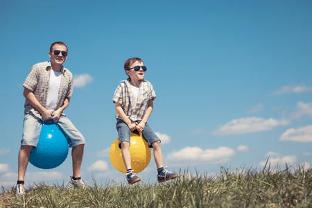 Father and son playing on the field at the day time. People having fun outdoors. They jumping on inflatable balls on the lawn. Concept of friendly family.の写真素材