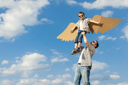 Father and son playing with cardboard toy wings in the park at the day time. Concept of friendly family. People having fun outdoors. Picture made on the background of blue sky.の写真素材