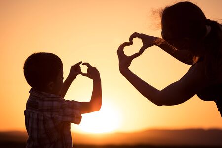 Mother and son walking on the field at the sunset time. People having fun outdoors. Concept of friendly family.の写真素材