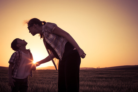 Mother and son walking on the field at the sunset time. People having fun outdoors. Concept of friendly family.の写真素材