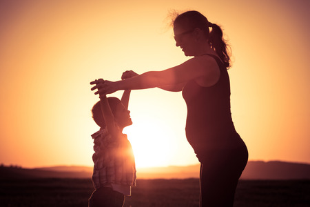 Mother and son walking on the field at the sunset time. People having fun outdoors. Concept of friendly family.の写真素材