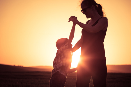 Mother and son walking on the field at the sunset time. People having fun outdoors. Concept of friendly family.の写真素材