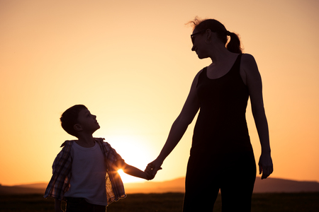 Mother and son walking on the field at the sunset time. People having fun outdoors. Concept of friendly family.の写真素材