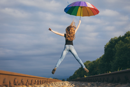 Teen girl with umbrella jumping on the railway at the day time. Concept of happiness.の写真素材