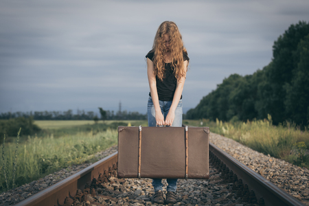Portrait of young sad ten girl standing with suitcase outdoors  on the railway at the day time. Concept of sorrow.の写真素材