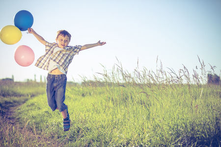 Happy little boy playing on road at the day time. He running in the field and holding in hands  balloons. Kid having fun on the nature. Concept of happiness.の写真素材