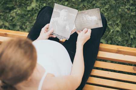 Pregnant woman sitting on the bench and looking at hildren's photos at the day time. Concept of happy expectation.の写真素材