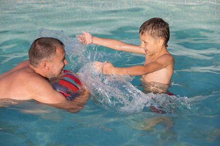Father and son  playing in the swimming pool at the day time. People having fun outdoors.  Concept of happy family.の写真素材