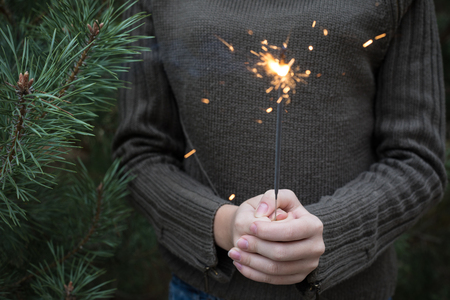 tenager with Bengal fire in hand standing near Christmas tree. New Year, Christmas mood.