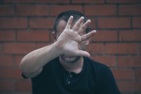 portrait one sad man standing near a wall and covers his face at the dayの写真素材