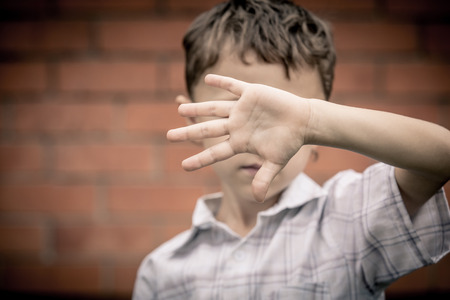 portrait one sad little boy standing near a wall  at the day time. Concept of sorrow.の写真素材