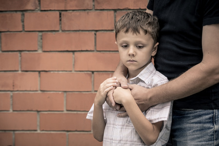 Portrait of young sad little boy and father sitting outdoors at the day time. Concept of sorrow.の写真素材