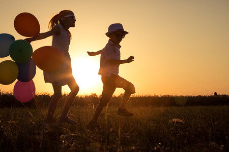 Silhouette of two happy children which playing on the field at the sunset time. They having fun on the nature.の写真素材