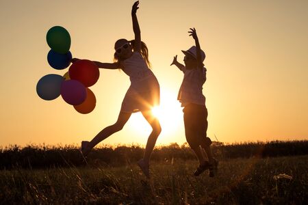 Silhouette of two happy children which playing on the field at the sunset time. They having fun on the nature.の写真素材