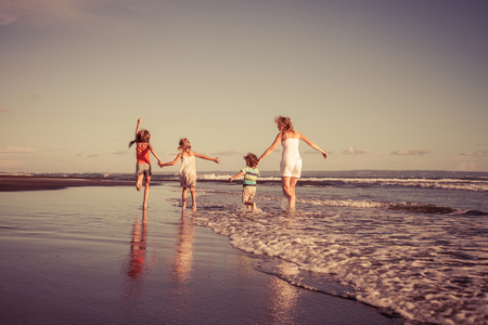 Mother and children running on the beach at the day time. Concept of friendly family on vacation.の写真素材