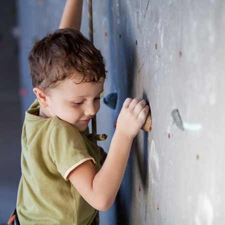 little boy climbing a rock wall indoor. Concept of sport life.の写真素材