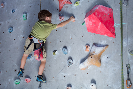 little boy climbing a rock wall indoor. Concept of sport life.の写真素材