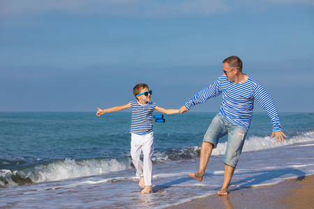 Father and son running on the beach at the day time. They are dressed in sailor's vests. Concept of sailors on vacation and friendly family.の写真素材