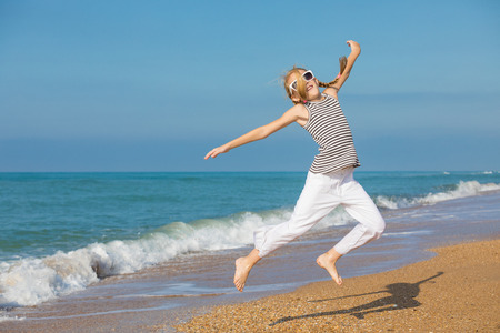 One happy little girl playing on the beach at the day time. She are dressed in sailor's vest. Kid having fun outdoors. Concept of sailor on vacation.の写真素材