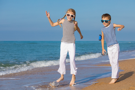 Two happy little children playing on the beach at the day time. They are dressed in sailor's vests. Kids having fun outdoors. Concept of sailors on vacation and friendly family.の写真素材