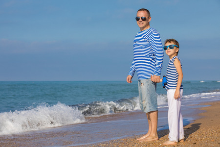 Father and son playing on the beach at the day time. They are dressed in sailor's vests. Concept of sailors on vacation and friendly family.の写真素材