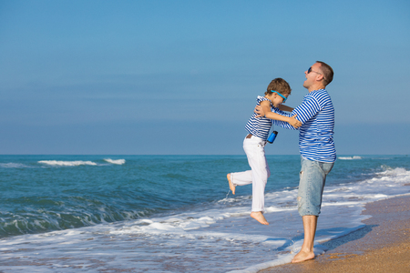 Father and son playing on the beach at the day time. They are dressed in sailor's vests. Concept of sailors on vacation and friendly family.の写真素材