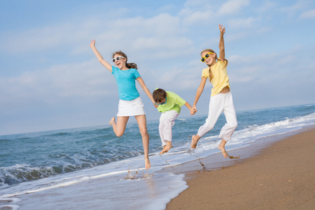 Three happy children running on the beach at the day time. People having fun outdoors. Concept of friendly family and of summer vacation.の写真素材