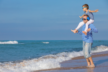 Father and son playing on the beach at the day time. They are dressed in sailor's vests. Concept of sailors on vacation and friendly family.の写真素材