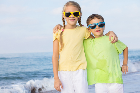 Two happy little children playing on the beach at the day time.  Kids having fun outdoors. Concept of summer vacation and friendly family.の写真素材