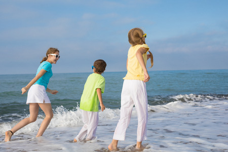 Three happy children running on the beach at the day time. People having fun outdoors. Concept of friendly family and of summer vacation.の写真素材