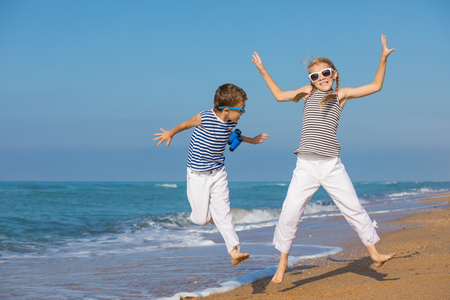 Two happy children playing on the beach at the day time. They are dressed in sailor's vests. Concept of sailors on vacation and friendly family.の写真素材