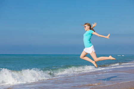 One teen girl jumping on the beach at blue sea shore in summer vacation at the day time. Kid having fun outdoors. Concept of happiness.の写真素材