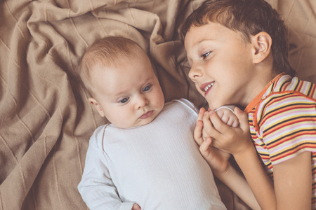 little boy playing with newborn on the bed  at the day timeの写真素材