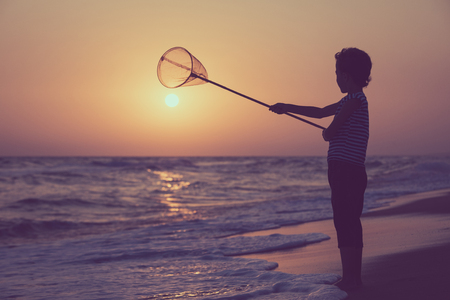 One happy little boy playing on the beach at the sunset time.  Kid having fun outdoors. Concept of summer vacation.の写真素材