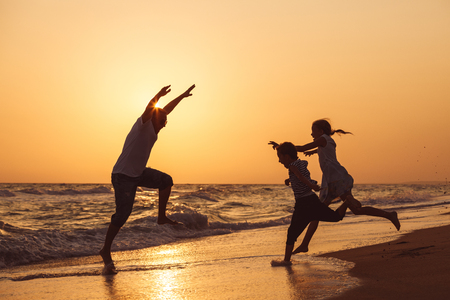 Father son and daughter playing on the beach at the sunset time. People having fun outdoors. Concept of summer vacation and friendly family.の写真素材