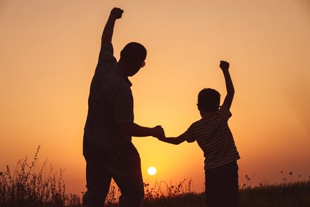 Father and son playing in the park at the sunset time. People having fun on the field. Concept of friendly family and of summer vacation.の写真素材