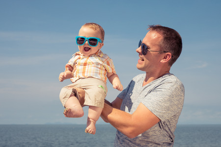Father and baby son playing on the beach at the day time. People having fun outdoors. Concept of summer vacation and friendly family.の写真素材