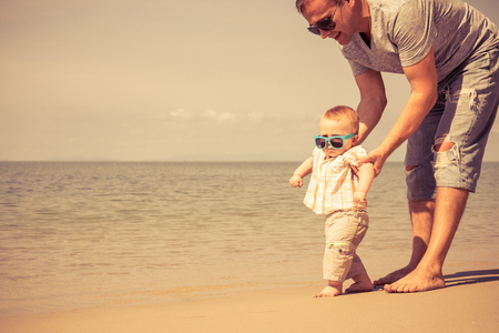 Father and baby son playing on the beach at the day time. People having fun outdoors. Concept of summer vacation and friendly family.の写真素材
