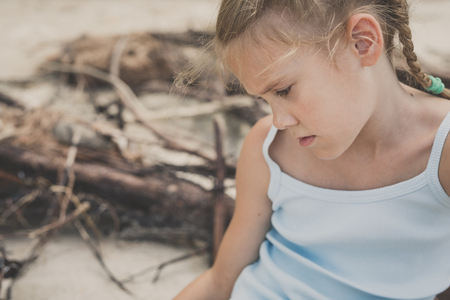 Portrait of one sad little girl. Child sitting on the beach at the day time. Concept of sorrow.の写真素材