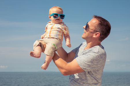 Father and baby son playing on the beach at the day time. People having fun outdoors. Concept of summer vacation and friendly family.の写真素材