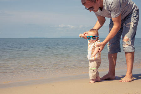 Father and baby son playing on the beach at the day time. People having fun outdoors. Concept of summer vacation and friendly family.の写真素材