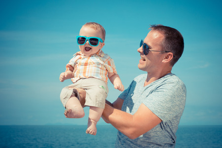 Father and baby son playing on the beach at the day time. People having fun outdoors. Concept of summer vacation and friendly family.の写真素材