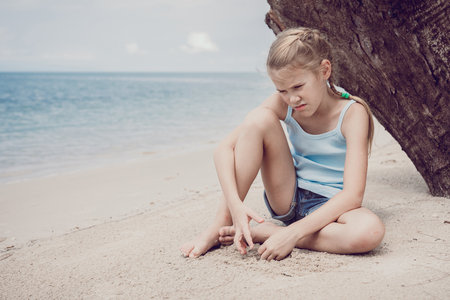 Portrait of one sad little girl. Child sitting on the beach at the day time. Concept of sorrow.の写真素材