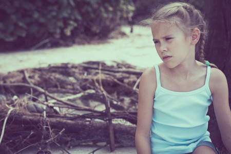 Portrait of one sad little girl. Child sitting on the beach at the day time. Concept of sorrow.の写真素材