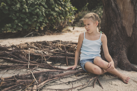 Portrait of one sad little girl. Child sitting on the beach at the day time. Concept of sorrow.の写真素材