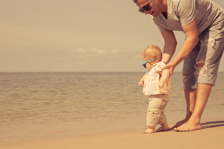 Father and baby son playing on the beach at the day time. People having fun outdoors. Concept of summer vacation and friendly family.の写真素材