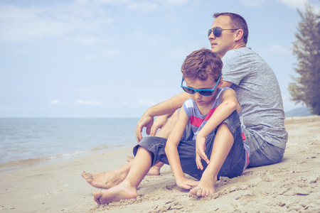 Portrait of young sad little boy and father sitting outdoors  on the beach at the summer day time. Concept of sorrow.の写真素材