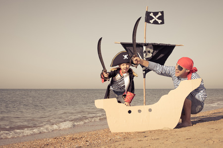 Father and son playing on the beach at the day time. They are dressed in sailor's vests and pirate costumes. Concept of happy game on vacation and friendly family.の写真素材