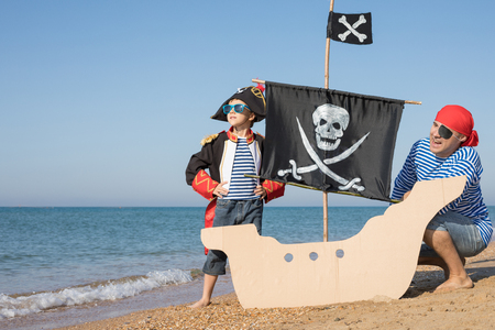 Father and son playing on the beach at the day time. They are dressed in sailor's vests and pirate costumes. Concept of happy game on vacation and friendly family.の写真素材